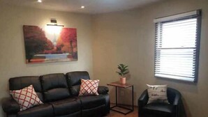 Ein Wohnzimmer mit einem schwarzen Ledersofa, einem kleinen schwarzen Sessel, einem Couchtisch aus Holz mit einer Pflanze und einem Gemälde an der Wand.