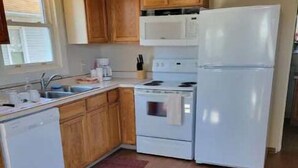 A compact kitchen with wooden cabinets, a white stove, a refrigerator, and a sink.
