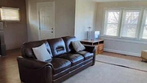 A living room with a dark brown leather sofa, a light-colored rug, and wooden flooring.