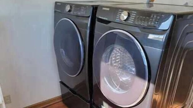 A pair of stacked front-loading washing machines in a room with wooden flooring and a white wall.