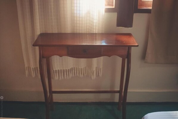 A wooden table with a drawer in a room with a green carpet and a window with curtains. - Pousada Hannah (Prado)