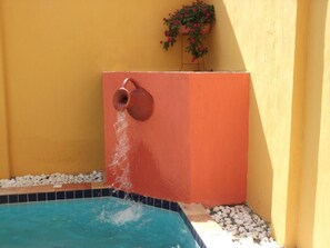 A swimming pool with a water feature, surrounded by white pebbles and a yellow wall. - Pousada Hannah (Prado)