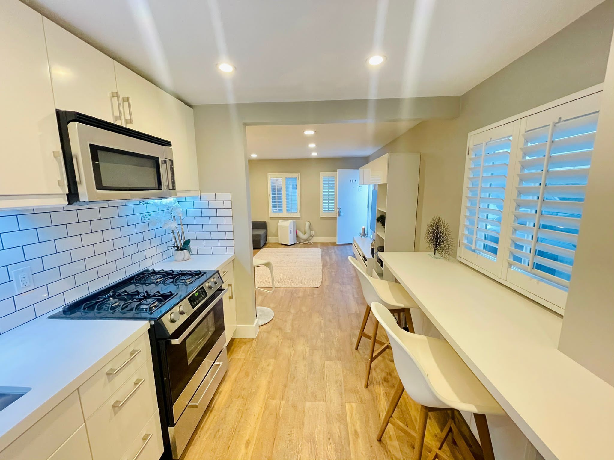 A modern kitchen with white cabinets, a gas stove, and a microwave. There is a dining area with a white table and chairs.