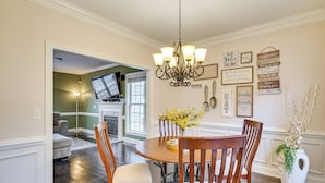 A dining area with a chandelier, wooden chairs, a round table, and a vase of flowers. - Wendell Home w/ Fenced Yard, Close to Raleigh (Wendell)