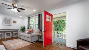 A living room with a sofa, a coffee table, a red door, and a view of the outdoors. - Enjoy the Fall & Winter Months in This Charming Home in Beautiful Marietta  (Marietta)
