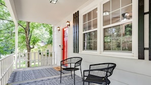 A porch with two black chairs, a red door, and a large window with a ceiling fan. - Enjoy the Fall & Winter Months in This Charming Home in Beautiful Marietta  (Marietta)