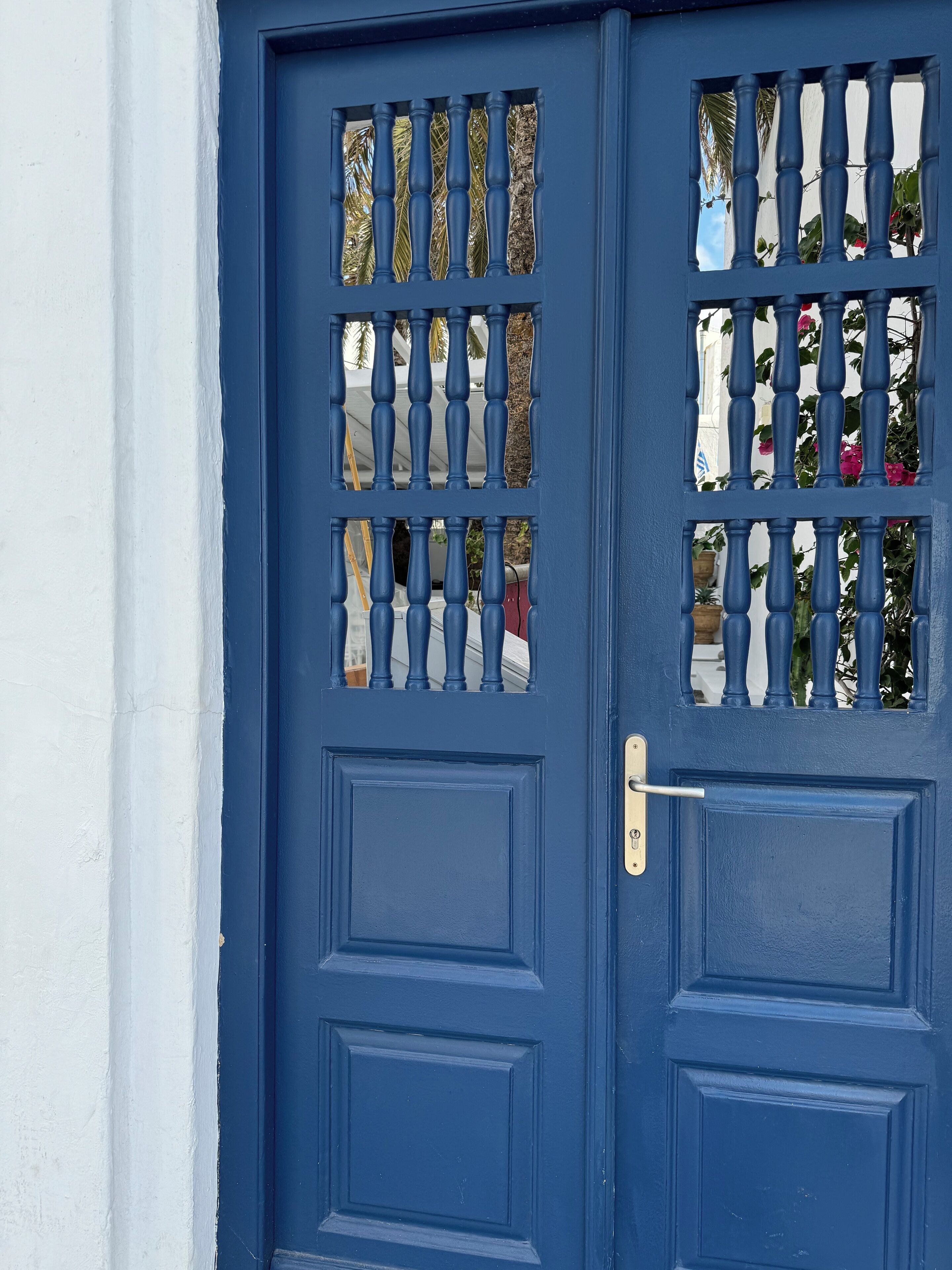 Une porte bleue avec une poignée en métal et un trou de serrure, ornée d’un panneau de verre décoratif représentant un palmier et des fleurs.
