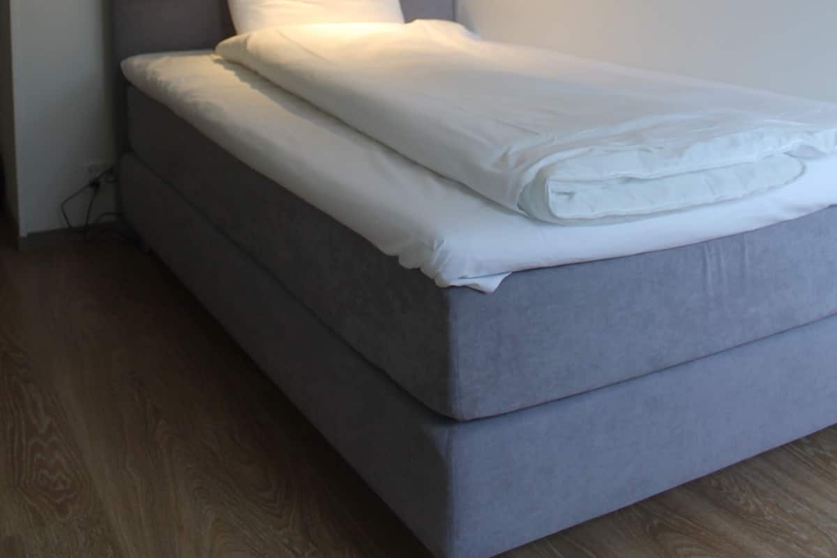 A single bed with a headboard, a bedside lamp, and a wooden floor.