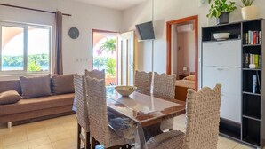 A spacious living area with a dining table, chairs, a sofa, a bookshelf, and a ceiling fan.