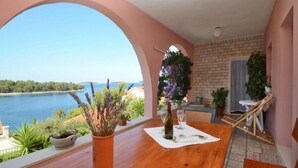 A balcony with a view of a lake, a wooden table with a bottle and glasses, and potted plants.