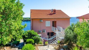 A pink villa with a red-tiled roof, a staircase leading to a balcony, and a view of the sea.