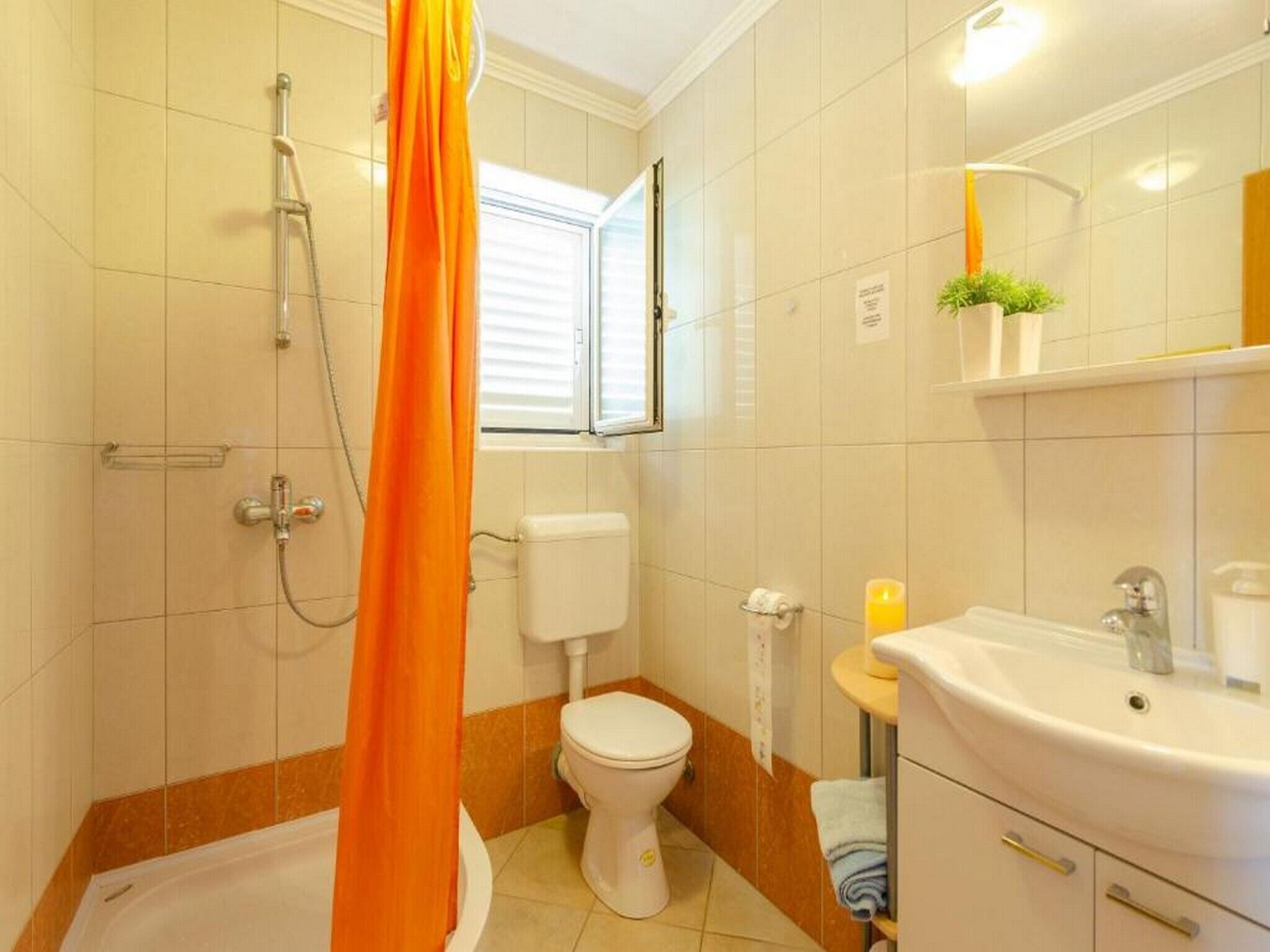 Een badkamer met douche, toilet, wastafel en een raam.