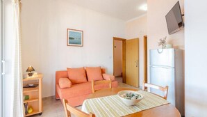 Un salon confortable avec un canapé, une table à manger et des chaises, un téléviseur fixé au mur et un réfrigérateur.