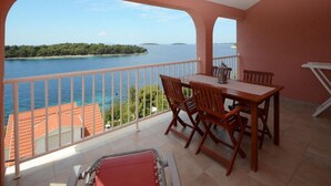 Un balcon avec une table et des chaises, donnant sur une étendue d’eau et une île lointaine.