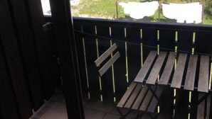 Un balcón con una mesa y sillas de madera, vista a un área boscosa y una cerca verde al fondo.