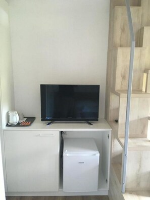 Una pequeña kitchenette con un refrigerador blanco, un televisor de pantalla plana negra y una cafetera en la encimera.