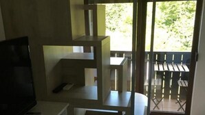 Un espacio habitable moderno y funcional con televisión integrada, un refrigerador pequeño y un balcón con mobiliario exterior.