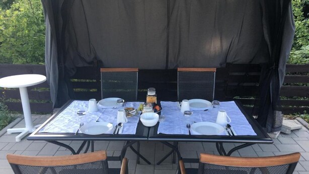 Un espace de restauration en plein air avec une table dressée pour quatre personnes, entourée de chaises, et une petite table placée sur le côté.