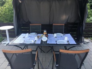 An outdoor dining area with a table set for four, surrounded by chairs, and a small table to the side.