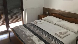 Un lit bien fait, avec des draps blancs et un couvre-lit à motifs, une tête de lit en bois, une table de chevet avec une lampe et un tableau encadré au mur.