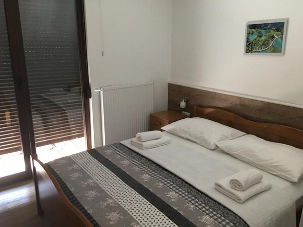 Ein ordentlich bezogenes Bett mit weißen Leinentüchern und einer gemusterten Tagesdecke, ein hölzerner Kopfseitenverkleidung, ein Nachttisch mit Lampe und ein gerahmtes Bild an der Wand.