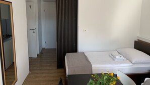 Une chambre d’hôtel avec un lit, une petite table sur laquelle est posé un vase de fleurs, un miroir et une porte donnant sur un couloir.