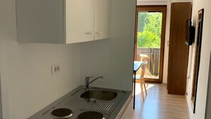 Une cuisine compacte dotée d’une cuisinière, d’un évier et de placards intégrés, qui donne sur un balcon avec une table et des chaises en bois.