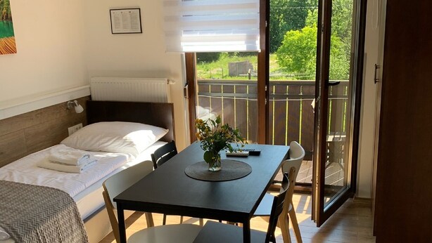 Une chambre avec un lit, une table et des chaises, un petit balcon et une vue sur la verdure.