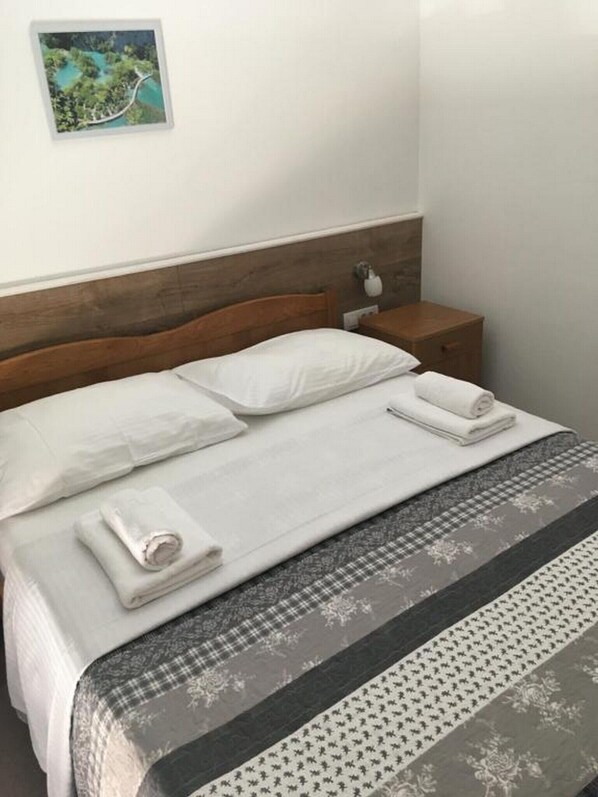 A neatly made bed with white linens, a wooden headboard, and a nightstand with a lamp.