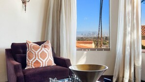 A living room with a dark brown sofa, a chessboard, and a view of a cityscape through a window with white curtains.