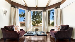 A room with two dark armchairs, a glass coffee table, and a view of trees through large windows.