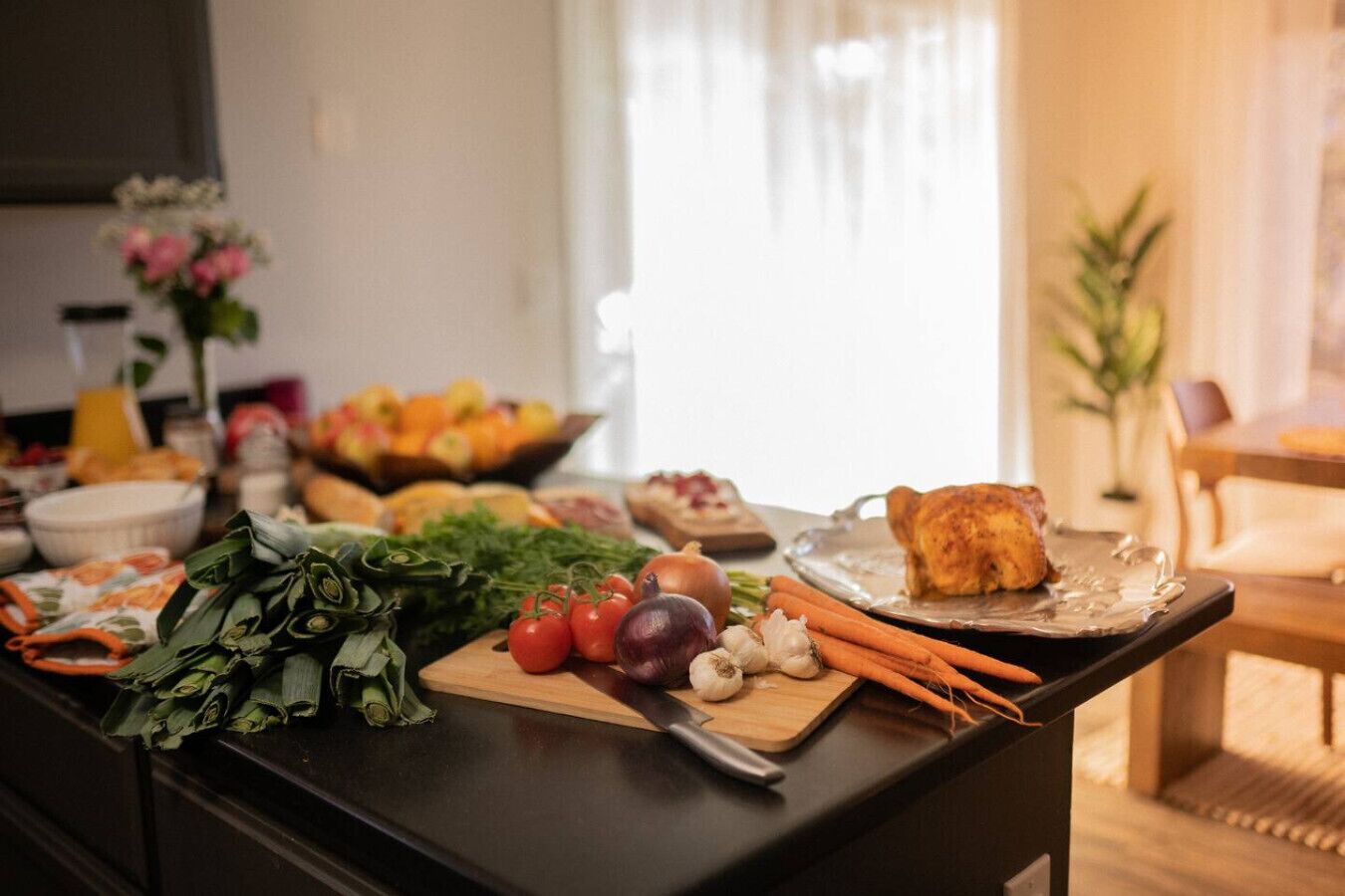 A kitchen counter with fresh vegetables, a cutting board, and a tray with a roasted chicken.