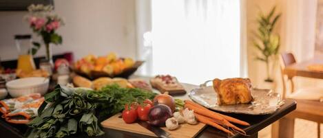 A kitchen counter with fresh vegetables, a cutting board, and a tray with a roasted chicken.
