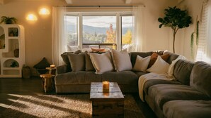 A cozy living room with a sectional sofa, a coffee table, and a large window with a view of trees. - Pool Sunset View Game Room Full Kitchen (Redding)