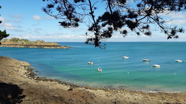 Un littoral rocheux bordé d’une eau turquoise cristalline, où plusieurs bateaux sont amarrés.