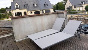 Un balcon doté d’une rambarde en métal et de deux fauteuils de jardin blancs.