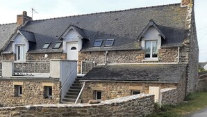 Un bâtiment en pierre doté d’un toit à forte pente, de nombreuses fenêtres et d’un escalier menant à un étage supérieur.