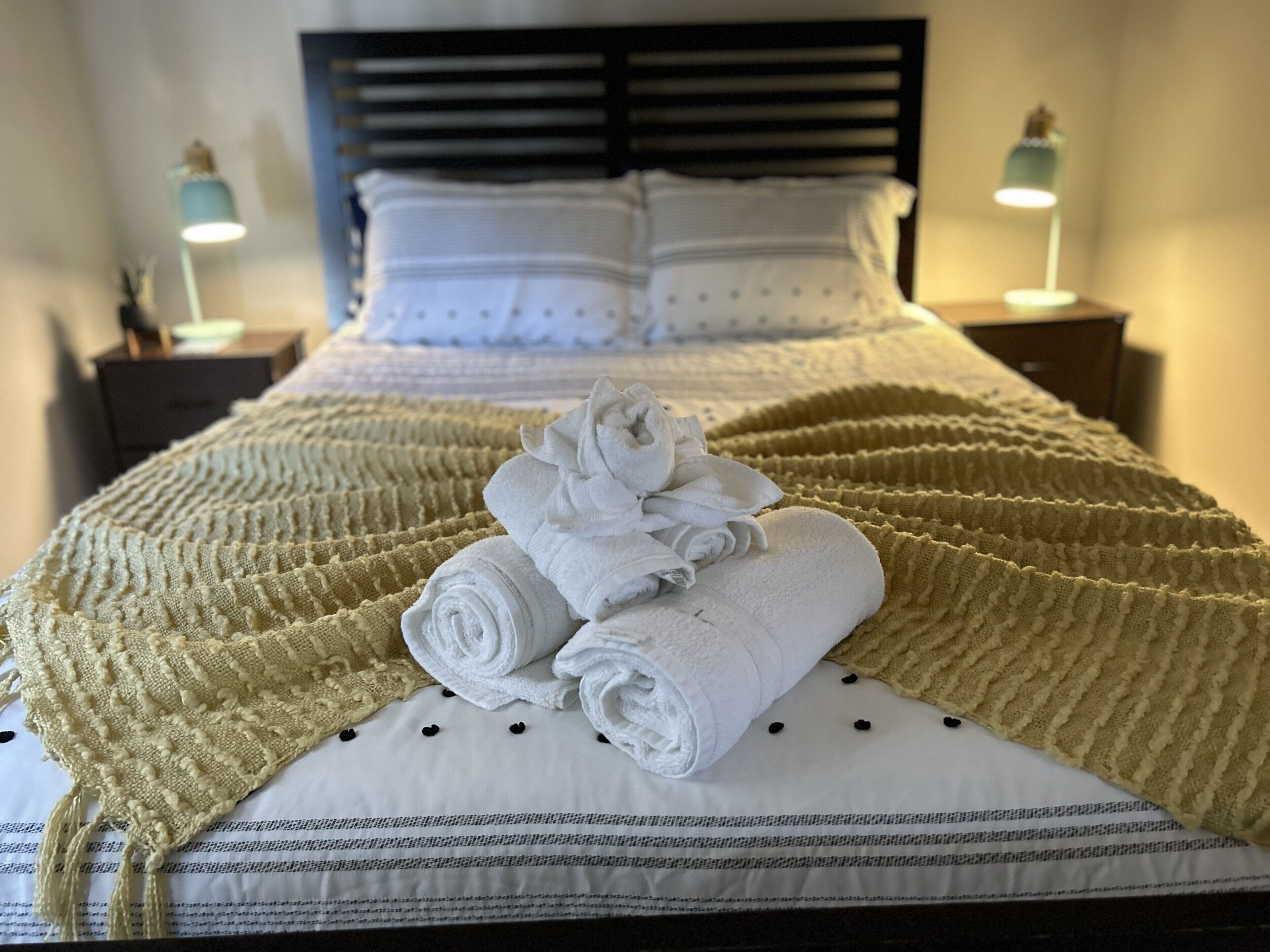 A neatly made bed with a rolled white towel and a beige blanket.
