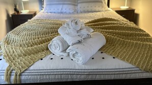 Un letto rifatto con cura, un asciugamano bianco arrotolato e una coperta beige.