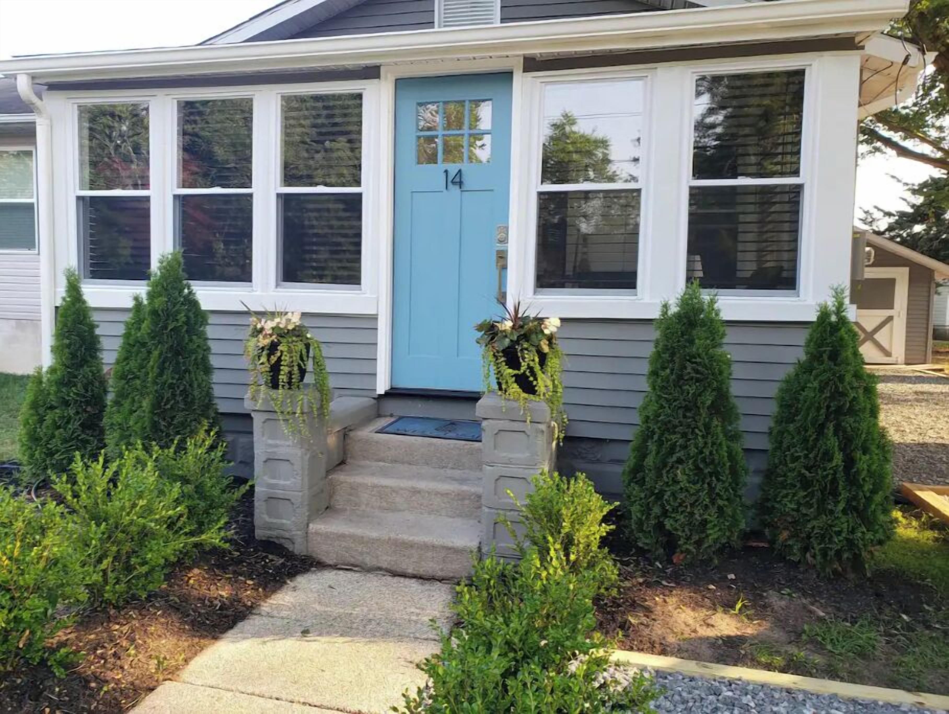 A house with a blue front door, number 14, and a small porch with steps leading up to it. There are two potted plants on either side of the door.