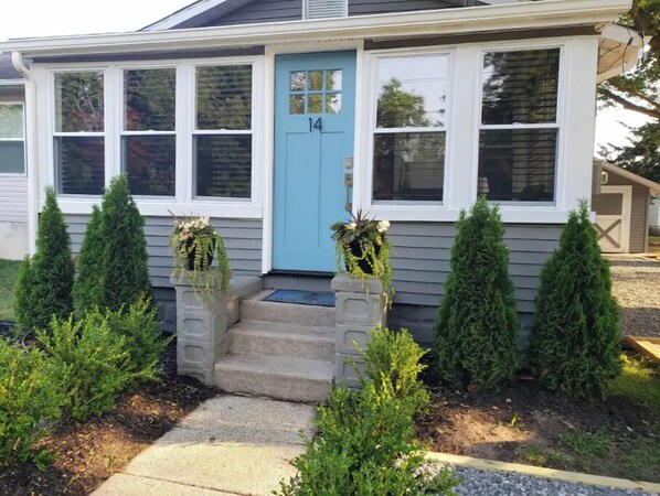 A house with a blue front door, number 14, and a small porch with steps leading up to it. There are two potted plants on either side of the door.