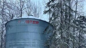 Uma estrutura metálica cilíndrica com a palavra 'WATER' visível na lateral, rodeada por neve e árvores.