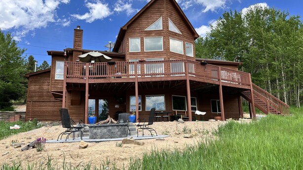 A two-story wooden cabin with a balcony, large windows, and a stone fireplace. - Private, Cozy, and Remote Mountain Apartment in Walk-Out Garden Level w/Patio. (Black Hawk)