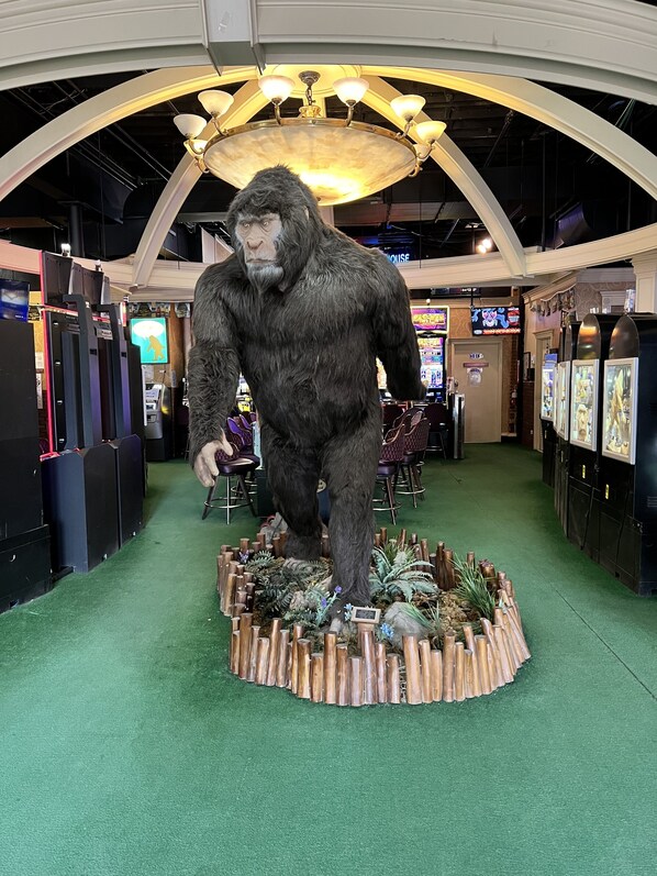 A large indoor exhibit featuring a life-sized gorilla statue on a platform surrounded by plants and wooden elements.