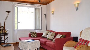 Ein gemütliches Wohnzimmer mit einem roten Sofa, einem Korbsessel, einem kleinen Tisch mit weißer Spitzenleinentischdecke und einer Stehlampe.