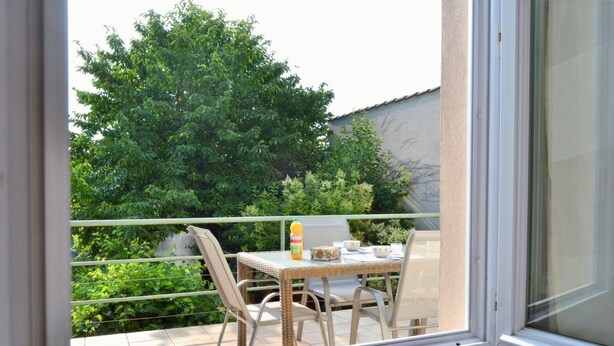 Ein Balkon mit Tisch und Stühlen, einer Orangensaftflasche und Blick auf einen grünen Baum sowie ein Gebäude im Hintergrund.