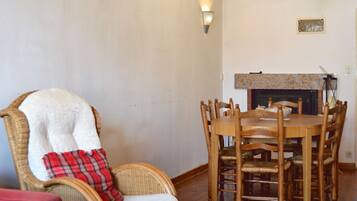 A dining area with a wooden table and chairs, a wicker chair with a plaid blanket, and a fireplace.