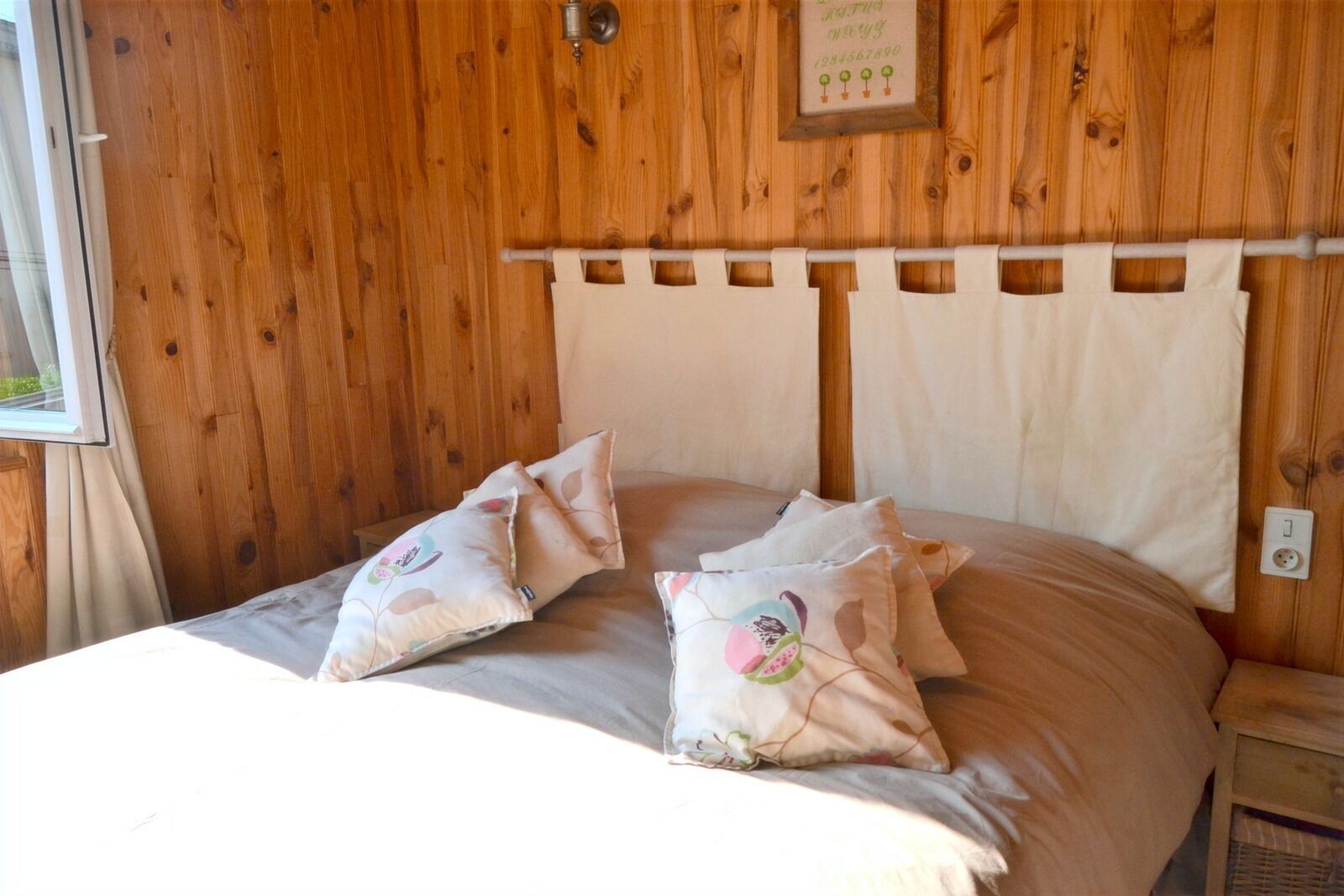Una habitación con paneles de madera, una cama con dos almohadones decorativos y un cabecero de diseño sencillo.