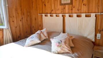 Una habitación con paneles de madera, una cama con dos almohadones decorativos y un cabecero de diseño sencillo.