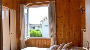 Ein Schlafzimmer mit Holzwand, einem fenster mit Vorhängen, einem Bett mit Kissen und einer Tür.